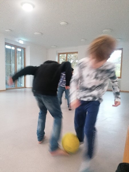 Zwei Kinder toben in einem Saal mit einem Ball. Ihre Umrisse sind wegen der Schnelligkeit verschwommen.