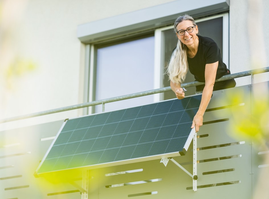 Eine Frau montiert ein Steckersolargerät am Balkon.