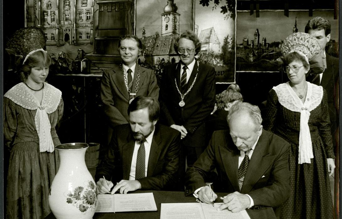 Schwarz-weiß Aufnahme von mehreren Personen, zwei Männer unterzeichnend sitzend Verträge