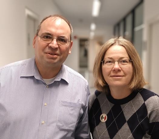 Porträt von zwei Personen; im Hintergrund ein Flur eines Bürogebäudes