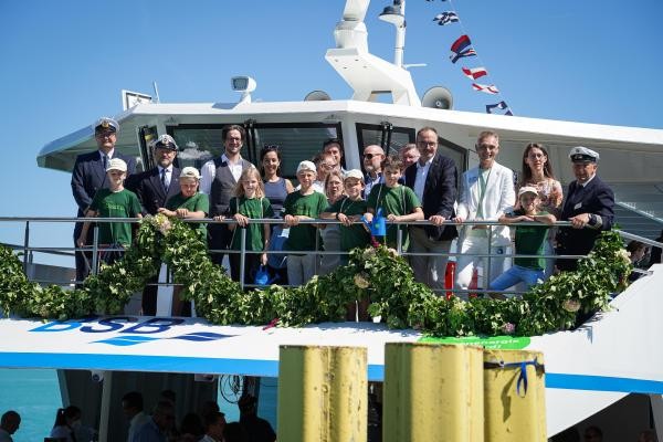 Eine Personengruppe steht an der geschmückten Reling eines Schiffes.