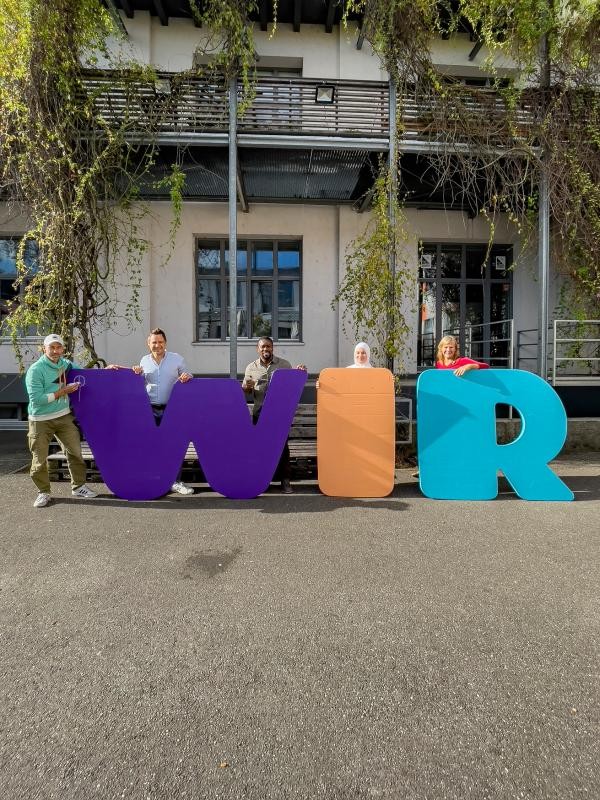 Personen stehen hinter bunten Buchstabenaufstellern, die das Wort "wir" bilden