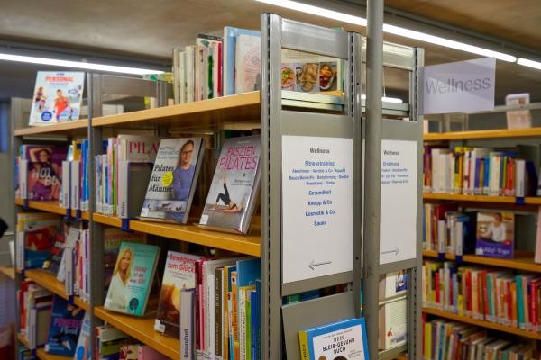 Blick in ein paar Reihen gefüllter Bücherregale. An den Fronten kleben Zettel mit Beschriftungen der jeweils enthaltenen Bücher.