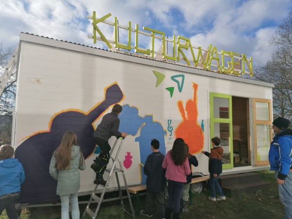 Kinder bemalen einen Bauwagen, auf dem "Kulturwagen" steht.