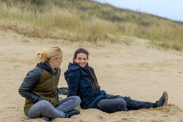 Zwei Frauen sitzen im Sand an einer Düne.