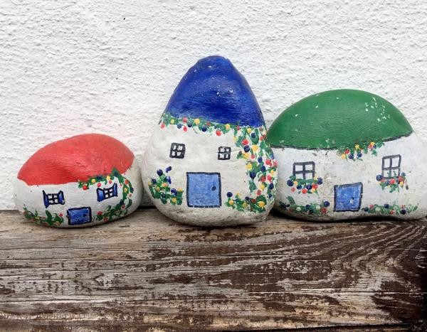 Symbolbild: Drei mit Häusern bemalte Steine auf einem Holzbalken